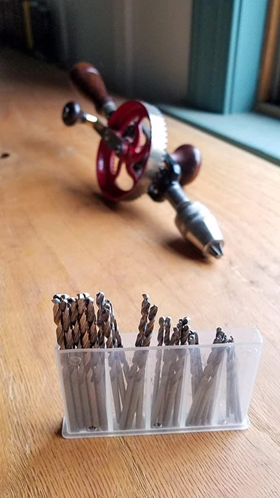Box Of New Rockler Drill Bits With A Millers Falls No. 5 Egg Beater Antique Hand Drill In The Background On A Woodworking Workbench
