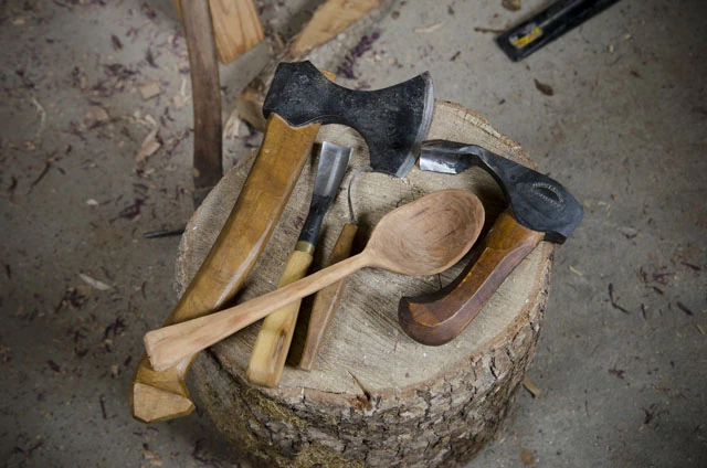 Green Woodworking Tools On A Stump, Including Carving Hatchet, Carving Gouge, Hook Knife, Bowl Adze, And Wooden Spoon