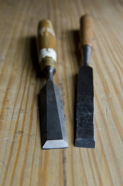 Two Antique Wood Chisels Sitting On A Woodworking Workbench: A Bevel Edge Bench Chisel And A Non Beveled Bench Chisel