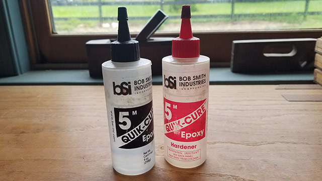 Two Bottles Of Quick-Cure 5 Minute Epoxy Sitting On A Woodworking Workbench
