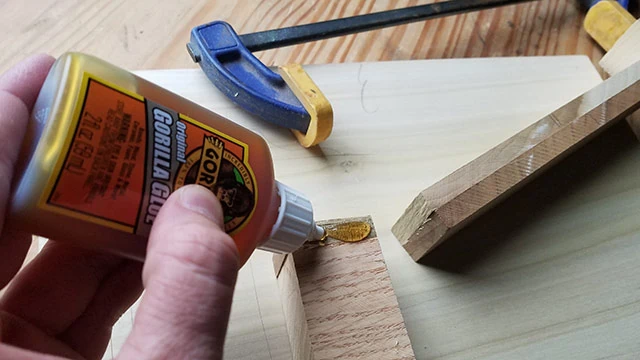 Gorilla Glue 2 Oz Bottle Polyurethane Glue Gluing A Broken Piece Of Wood With A Blue Clamp In The Background