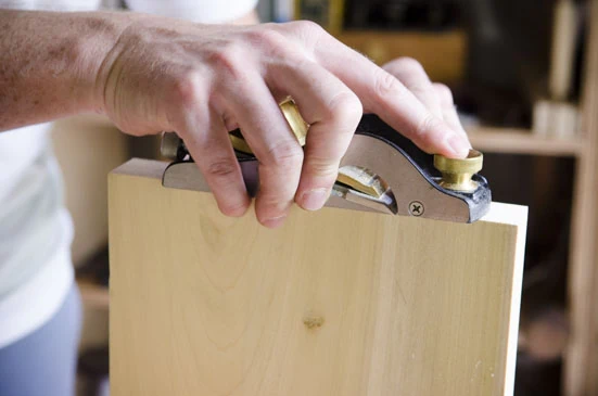 Joshua Farnsworth Using A Lie-Nielsen Rabbet Block Plane To Square The End Grain Of A Board While Squaring Up A Board For Woodworking On A Woodworking Workbench