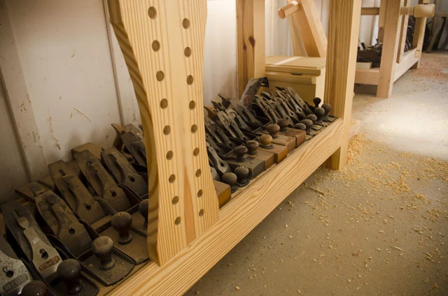 An Assortment Of Antique Bench Hand Planes Under A Woodworking Workbench