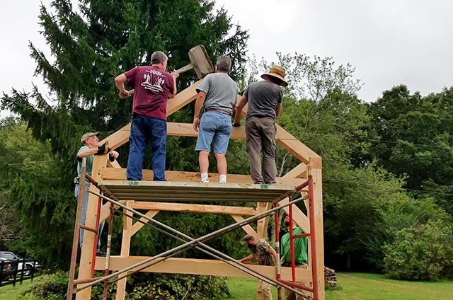 Students Of A Timber Framing Class Using A Large Mallet To Secure Roof