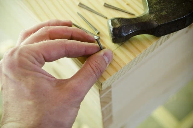 Woodworker Holding A Historical Style Cut Nail For Hammering A Wooden Desk Top