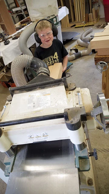 Boy Helping With Milling Wood On A Grizzly Thickness Planer In A Woodworking Shop