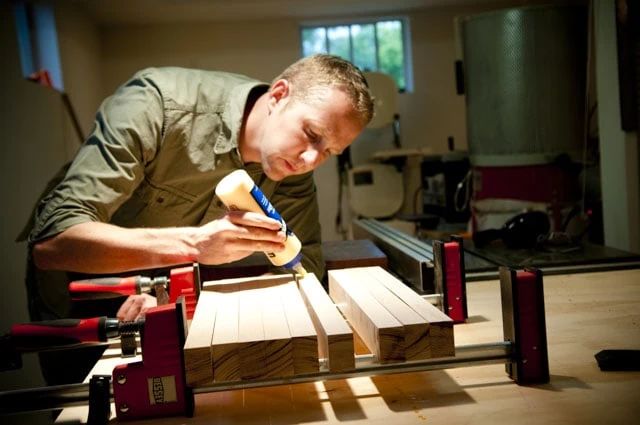 Woodworker Joshua Farnsworth Spreads Best Wood Glue On A Butcher Block Cutting Board With Woodworking Clamps
